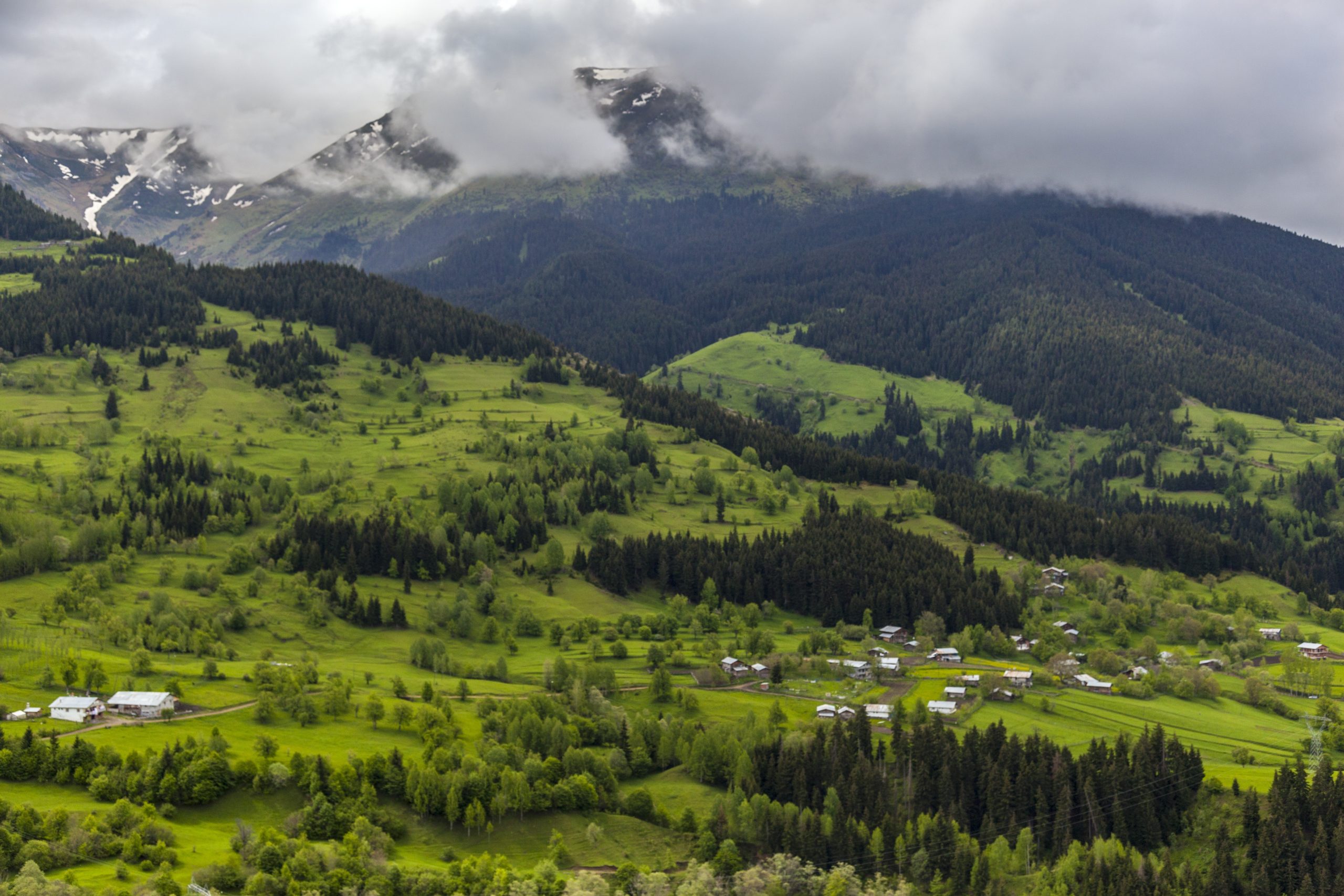 A landscape of hills covered in forests snow and fog under a cloudy sky at daytime